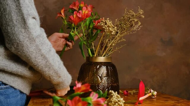 Young woman makes bouquet of flowers. Florist cuts stems of flowers, puts them in vase. Valentines day flower arrangement, festive home decor. 