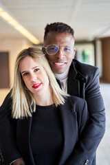 Glad African American man in glasses smiling and looking at camera while embracing blond woman during romantic date