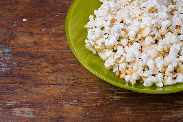 Pop corn in green plate on wooden table background. Closeup shot, place for text