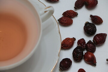 dried rosehip berries and rosehip tea in a white porcelain glass. Dog rose tea. Medicinal plants and herbs composition. Healthy drink concept.