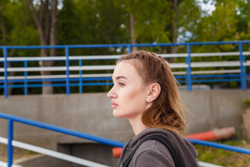 Fototapeta premium Portrait of young woman sidewards in sportswear with backpack going to stadium to make physical exercises.