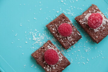 Raspberry and coconut zest on three pieces of chocolate cake. Blue background. Top view. Brownie