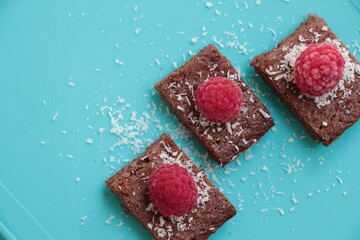 Raspberry and coconut zest on three pieces of chocolate cake. Blue background. Top view. Brownie