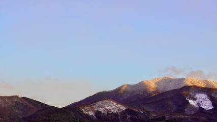 Fototapeta na wymiar 群馬県高山村の雪が積もり始めた山に夕日の光がオレンジ色にうつっている風景