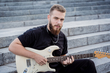 Young street musician playing guitar sitting on granite steps