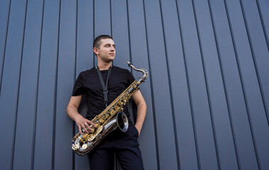Fototapeta premium Young street musician playing saxophone near the big blue wall