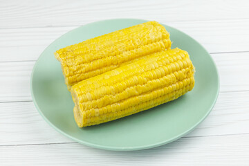 Two short boiled corn cobs on a green plate. Foods that reduce the risk of stroke, diabetes and cardiovascular disease.