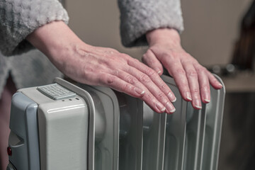 warm hands over an oil-filled mobile heater. It's cold at home, electricity is expensive.