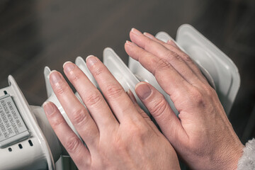 woman keeps hands warm over an oil-filled mobile heater. It's cold at home, electricity is expensive.