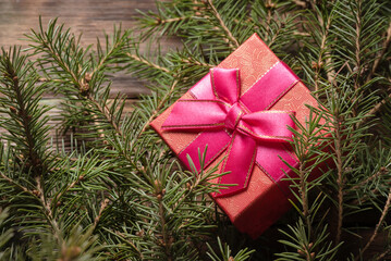 Red gift box with a ribbon in the fir tree branches background. Christmas background.