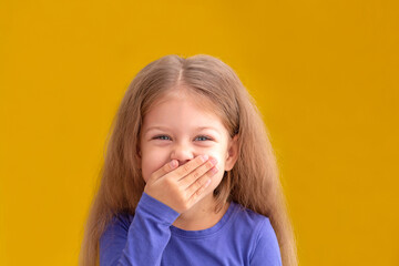 Portrait of laughing caucasian little girl child kid of 5 years looking at camera covering mouth by...