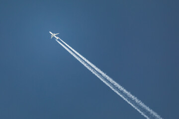 white plane with white contrail flies in the cloudless blue sky