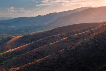 Mountain landscape at sunset with brightly lit hill tops in the foreground, Peloponnese, Greece
