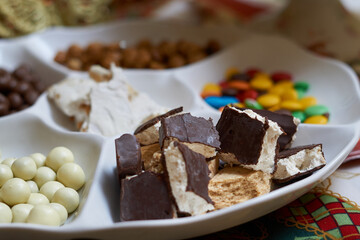 plate with Christmas sweets, sprinkles, caramelized peanuts and nougats in the foreground