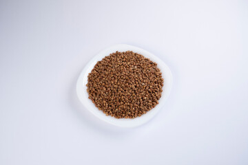 Buckwheat in a white plate on white background, top view. Healthy food. Cereals