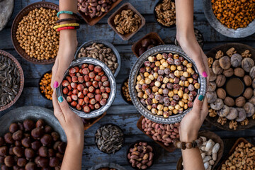Two bowls of hazelnut at the hands of two woman and assorted nuts at the background