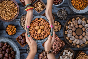 A bowl of almond at the hands of two woman and assorted nuts at the background