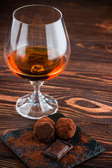 Glass of brandy and a chocolate truffles with chocolate on an old wooden table