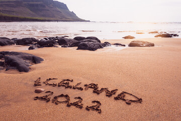 New year concept welcoming New Year 2022 written on a red sand beach with waves and red lava rocks on Iceland Ocean shore.