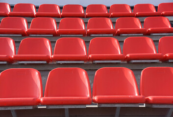 Plastic red chairs are arranged in straight rows in an empty sports stadium.