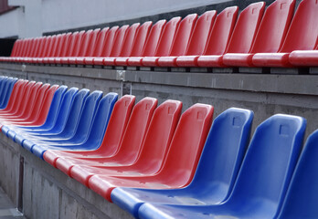 Fototapeta premium Plastic red and blue chairs are placed before the start of the match in an empty sports stadium.