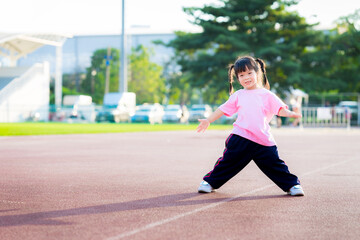 Child wearing pink t shirt is standing exercising. Kid smile and laugh, having fun making various gestures. Summer or spring evenings. Kindergarten children are 4 years old.