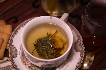 Holiday evening at home - porcelain cup of best herbal tea, antique candle in candlestick, old letters and jar of honey