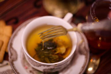 Holiday evening at home - porcelain cup of best herbal tea, antique candle in candlestick, old letters and jar of honey