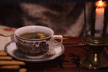 Holiday evening at home - porcelain cup of best herbal tea, antique candle in candlestick, old letters and jar of honey