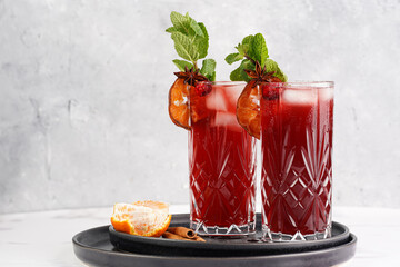 Traditional christmas beverage mulled wine with red cherry juice, orange tangerines, cinnamon sticks, ice cubes and anise on black trays
