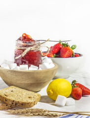 mermelada de fresa en tarro de cristal sobre marmol de cocina. decoracion ingredientes, fresas, azucar y limones