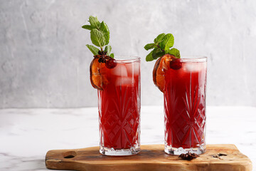 Traditional christmas beverage mulled wine with red cherry juice, orange tangerines, cinnamon sticks, ice cubes and anise on wooden board
