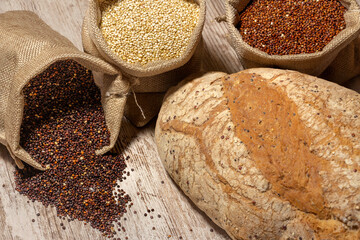 Quinoa bread with linen sacks stuffed with red, white and black quinoa, all on an old rustic wooden table. overhead view