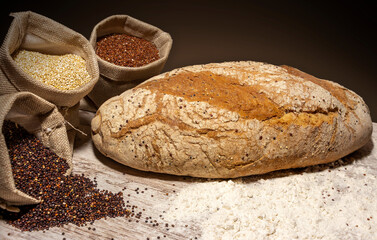 Quinoa bread with linen sacks filled with red, white and black quinoa, all on an old rustic wooden table. front view