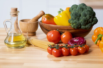 Group of fresh ripe tomatoes, peppers, and broccoli, bottle of olive oil and bunch of spaghetti on kitchen table