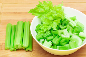 Fresh Chopped Celery Slices in White Bowl with Celery Sticks on Bamboo Cutting Board. Vegan and Vegetarian Culture. Raw Food. Healthy Diet with Negative Calorie Content