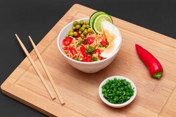 Beautiful Noodle Dish with Green Pea, Eggs, Red Hot Pepper, Greens and Lime with Chopsticks on Bamboo Cutting Board. Instant Noodles