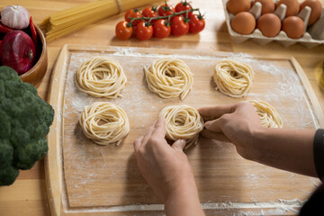 Hands of young woman cooking food from boiled spaghetti while rolling them on wooden board
