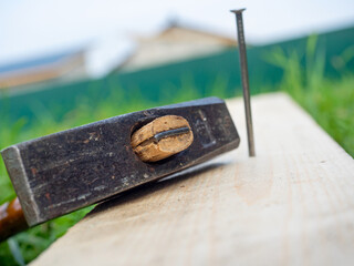 Close-up of an old hammer lying on a board. A nail driven into the board in the background. Cottage, worker, carpenter