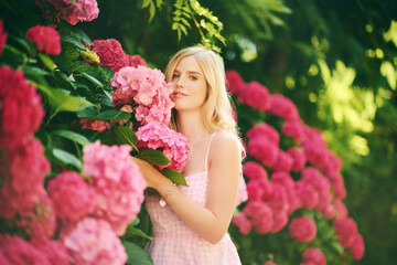 Outdoor portrait of young beautiful woman posing with hydrangea flowers in summer garden