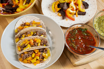 Plate with homemade mexican taco, tomato and pesto sauces and vegetable stew on wooden kitchen table