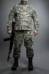 A man in an American camouflage uniform and army boots with a Kalashnikov assault rifle in his...