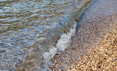 Colored pebbles  beach, motion blur of moving wave, crystal sea water.