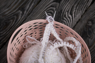 Obraz premium Knitting with needles. A skein of white thread and a fragment of a knitted product. Lie in a basket. On black pine boards. Close-up.