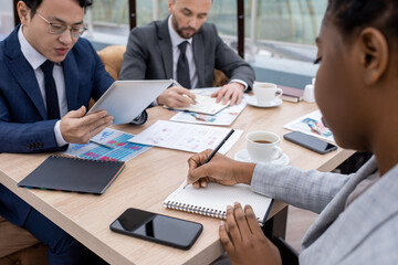 Young African businesswoman pointing at blank page of notebook while planning work in front of intercultural male colleagues