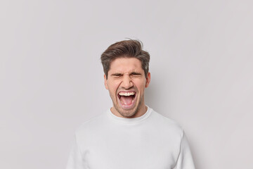 Portrait of emotional man screams from amazement keeps mouth wide opened yells loudly wears casual jumper isolated over white background. Excited male model reacts on awesome news or surprise