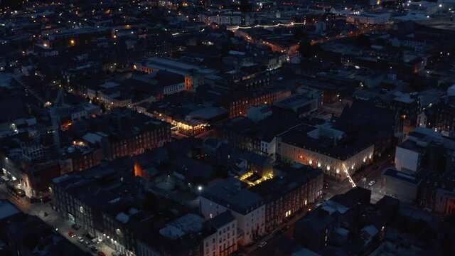 Fly above urban neighbourhood at night. Aerial view of buildings and streets lit by lights. Limerick, Ireland
