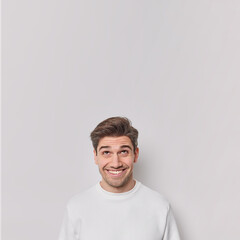 Happy curious European adult man smiles gladfully looks above sees something funny overhead focused up wears casual jumper isolated over white background blank copy space gazes at advertisement