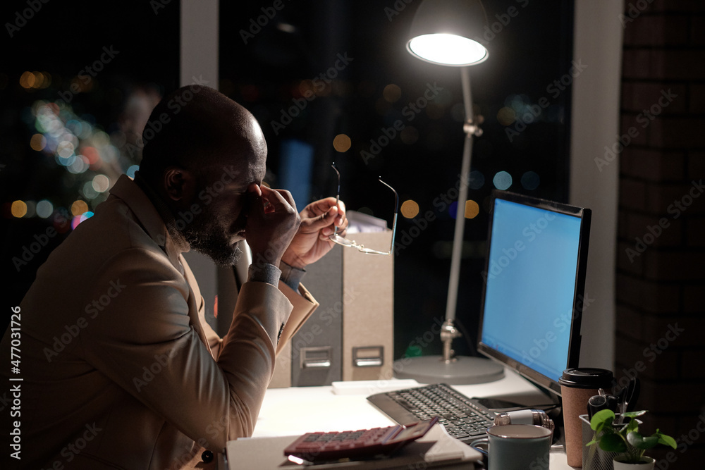 Poster young tired businessman touching his face while working in front of computer screen in office late a