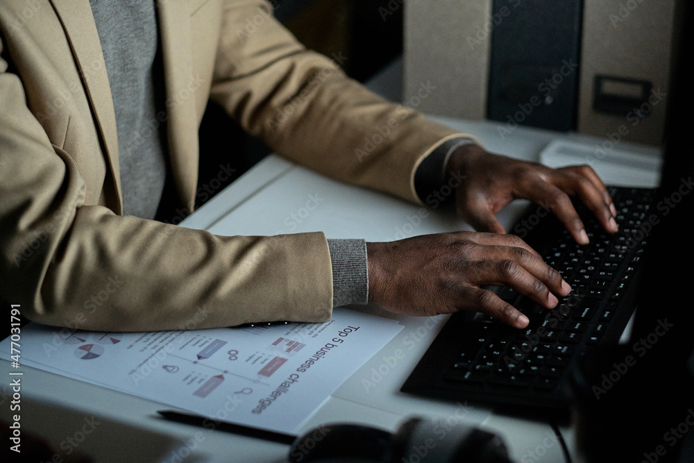Poster Hands of African businessman pressing keys of computer keypad while sitting by desk in front of monitor